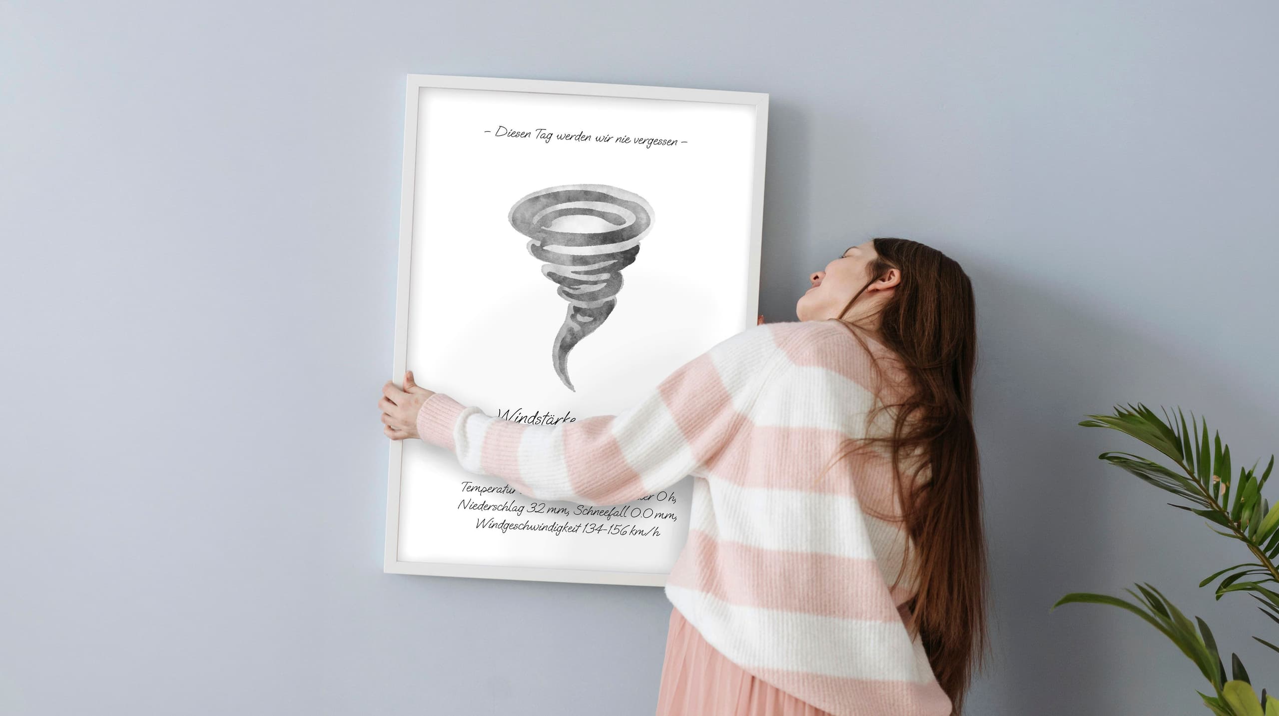 Picture of a young woman hanging a picture frame with a watercolour painting of a whirlwind